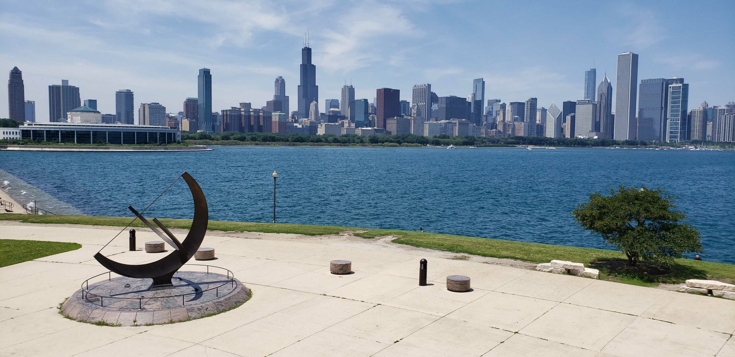 A photo facing northwest showing the Sundial Plaza and Man Enters the Cosmos sculpture with the city skyline in the background. Daytime photo.