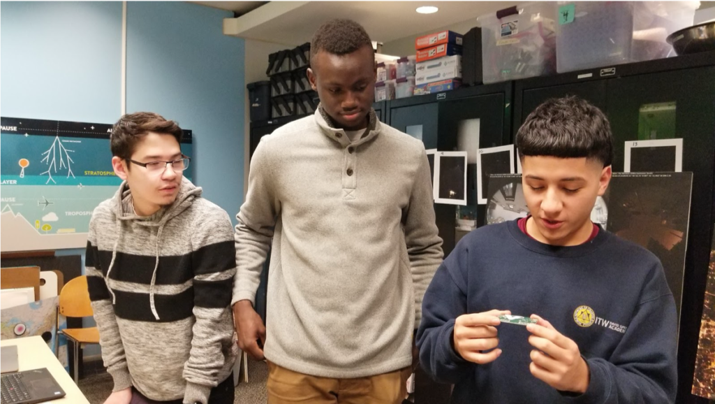 Gamaliel Cruz, Isaiah Meza, and Ibrahim Diop all observe the final ThinSat circuit board.