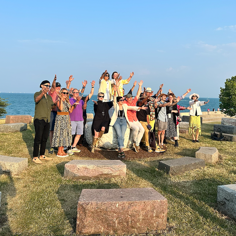 Denise Milan, one of the artists of Americas’ Courtyard, standing on the sculpture with friends, family, and fans. Their arms are raised up to the sky, in celebration of the solstice and the 25th anniversary of the sculpture. 