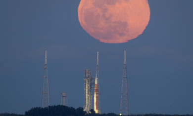 A bright orange full Moon rises behind a rocket on a launch pad at NASA’s Kennedy Space Center.