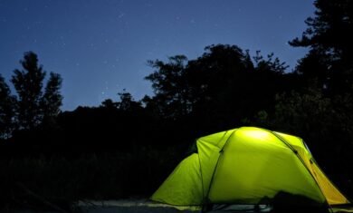 A green tent on sand with silhouetted trees and a blue night sky with stars