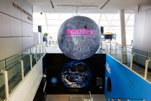A pink lowercase logo saying "beazley" is projected onto an oversized Moon globe suspended from the ceiling over the Adler Planetarium's south stairwell.