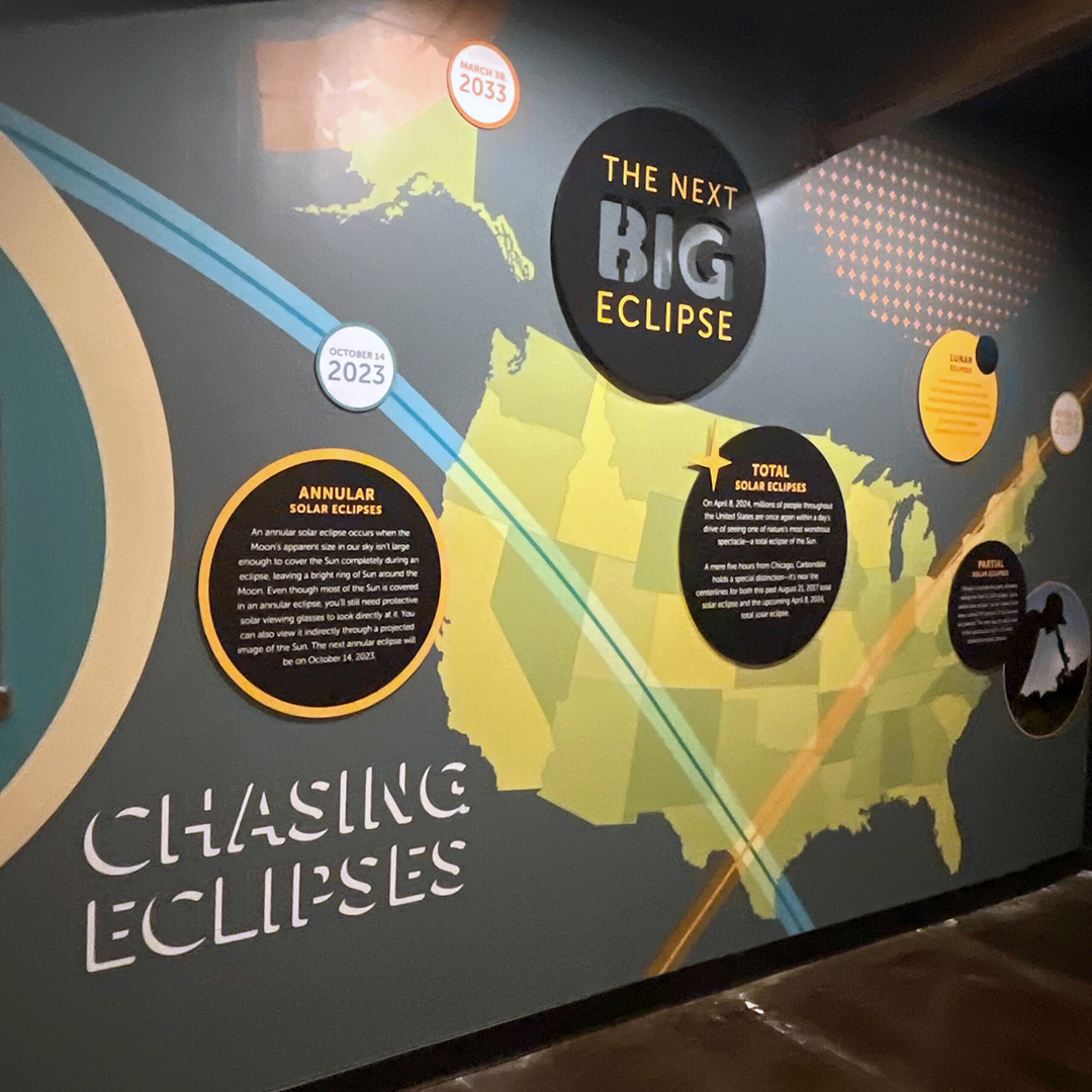 One of the walls in the temporary exhibit, Chasing Eclipses, at the Adler Planetarium in Chicago features the titles “Chasing Eclipses” and “The Next Big Eclipse” next to a large map of the United States.