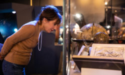 Woman examines a collection's object behind glass in the Chicago's Night Sky exhibition.