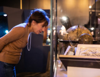 Woman examines a collection's object behind glass in the Chicago's Night Sky exhibition.
