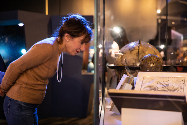 Woman examines a collection's object behind glass in the Chicago's Night Sky exhibition.