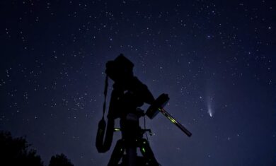 Camera attached to telescope shooting a comet in the night sky.