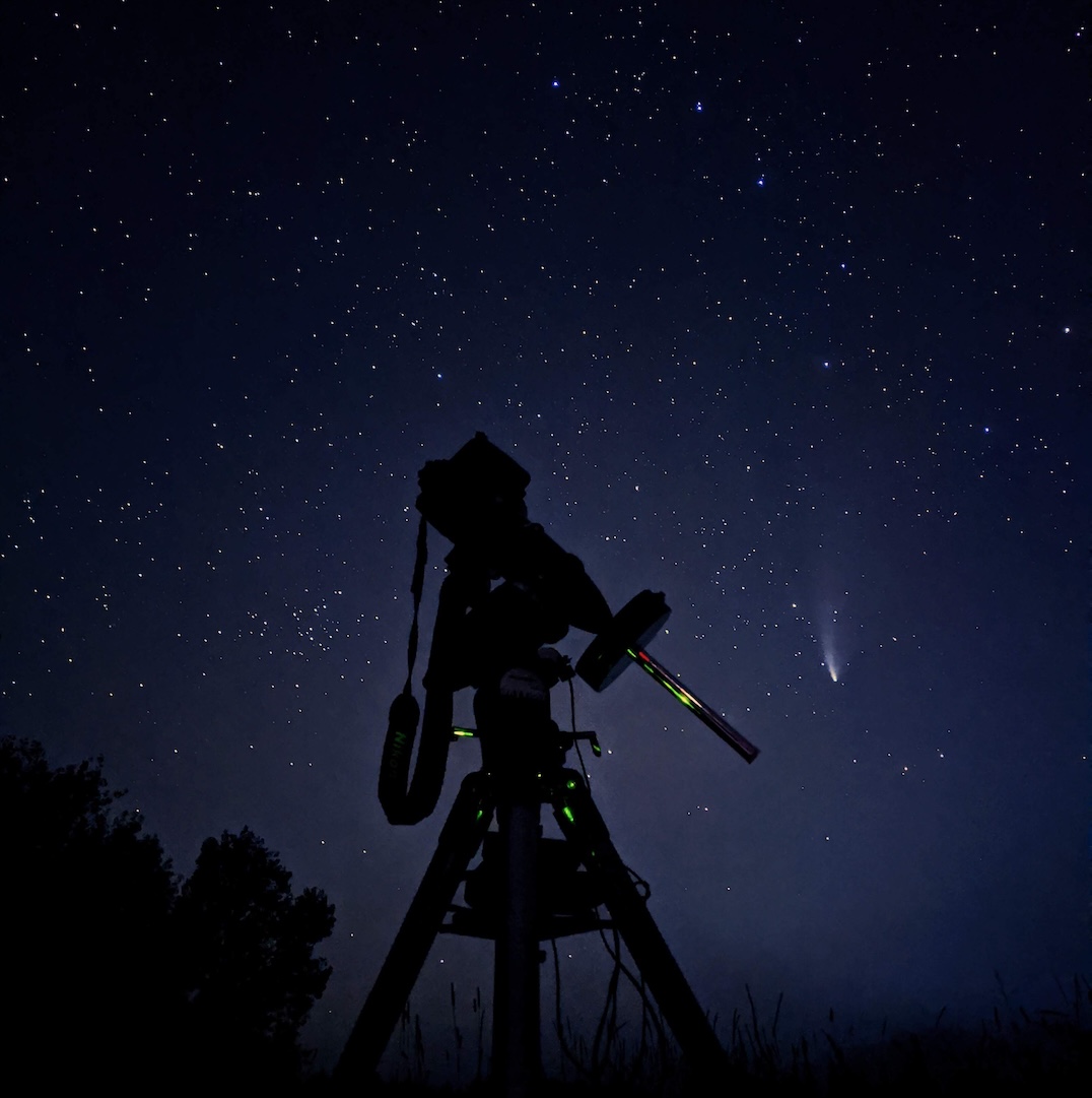 Camera attached to telescope shooting a comet in the night sky.