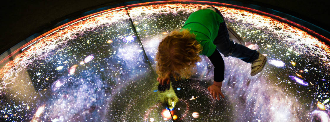 A child interacting with a lit-up cosmic floor display.