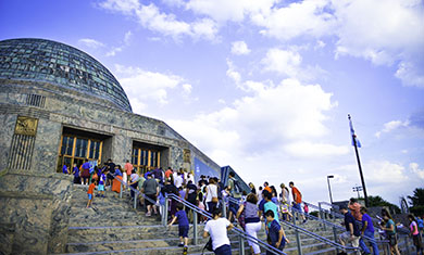 A large group of guests walk up the stairs of the Adler's main entrance.