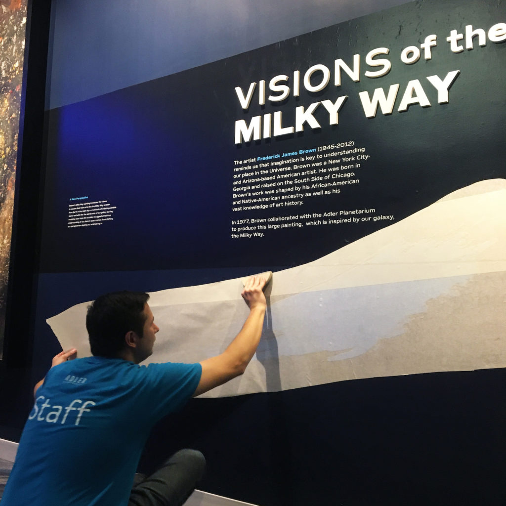 Neil Adam installing a graphic in Chicago’s Night Sky on a wall featuring Frederick J. Brown’s painting, “Milky Way.”