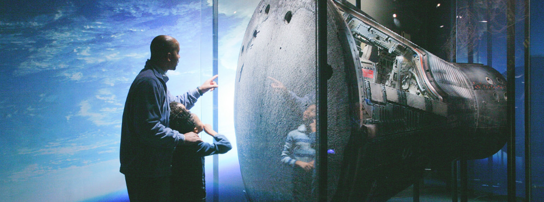 A father and son gazing at the Gemini 12 spacecraft, located in the Adler's "Mission Moon" exhibition.