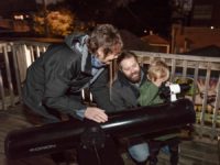 Adler telescope volunteer helps man and his child find stars and planets in the night sky through a telescope.