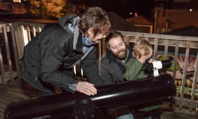 Adler telescope volunteer helps man and his child find stars and planets in the night sky through a telescope.