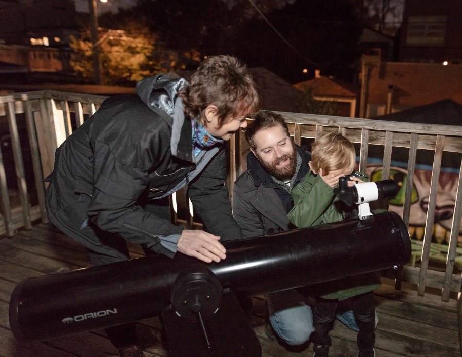 Adler telescope volunteer helps man and his child find stars and planets in the night sky through a telescope.