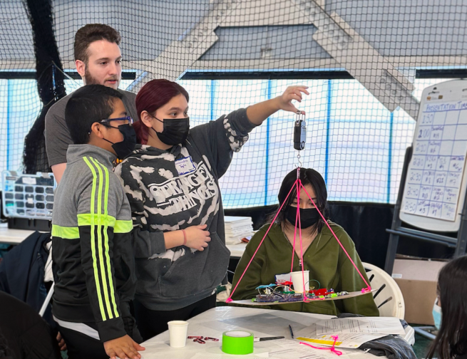 A group of students at the Adler Planetarium's 2023 Operation Airlift, weighing their airship with the guidance of an Adler STEM mentor.