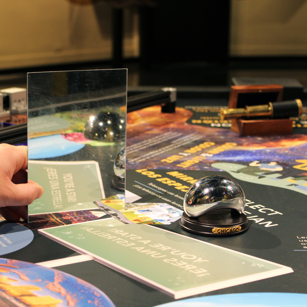 A hand holding a mirror on a table to show a reflection of a sign that says "You're A Star" and "¡Eres Una Estrella!"