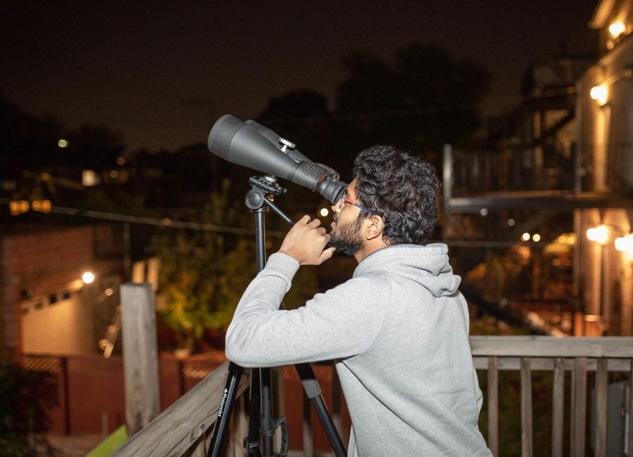 Man looking through a pair of telescopes into Chicago's night sky.