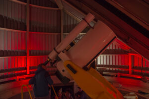 Person standing, looking through the large white telescope in the Doane Observatory at the Adler Planetarium.