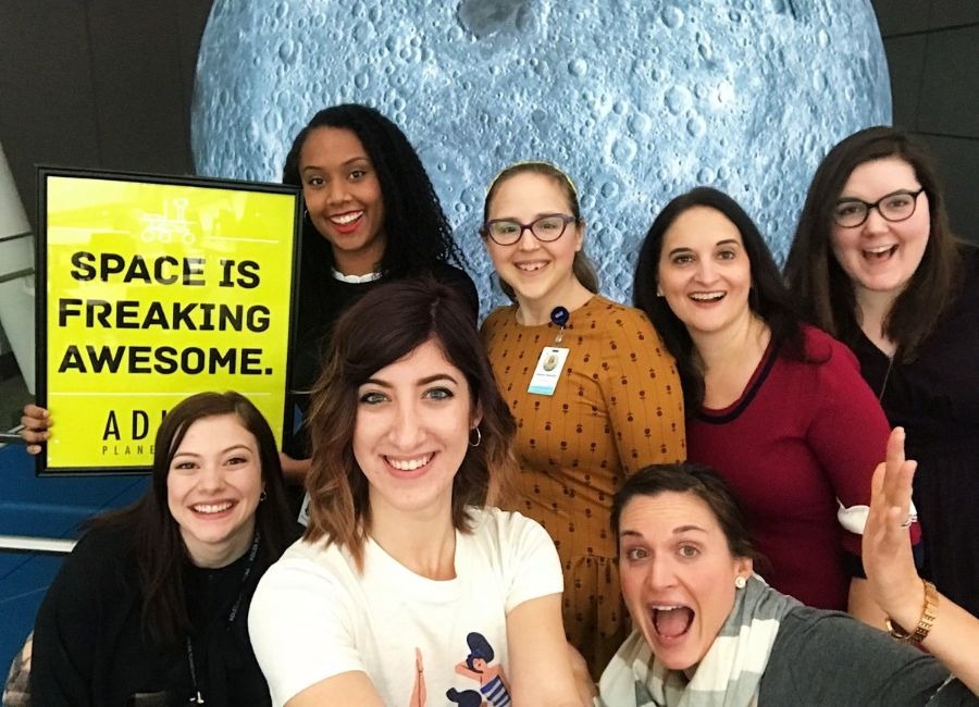 A group of Adler staff smile while posing in front of an inflatable Moon exhibition.