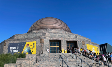 The Adler Planetarium on a sunny, summer day, with a line of guests on the museum steps.