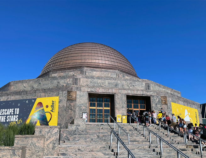 The Adler Planetarium on a sunny, summer day, with a line of guests on the museum steps.