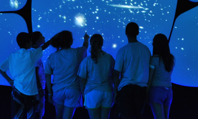 Students with their backs facing the camera point and take in the cosmic wall in the Universe exhibition