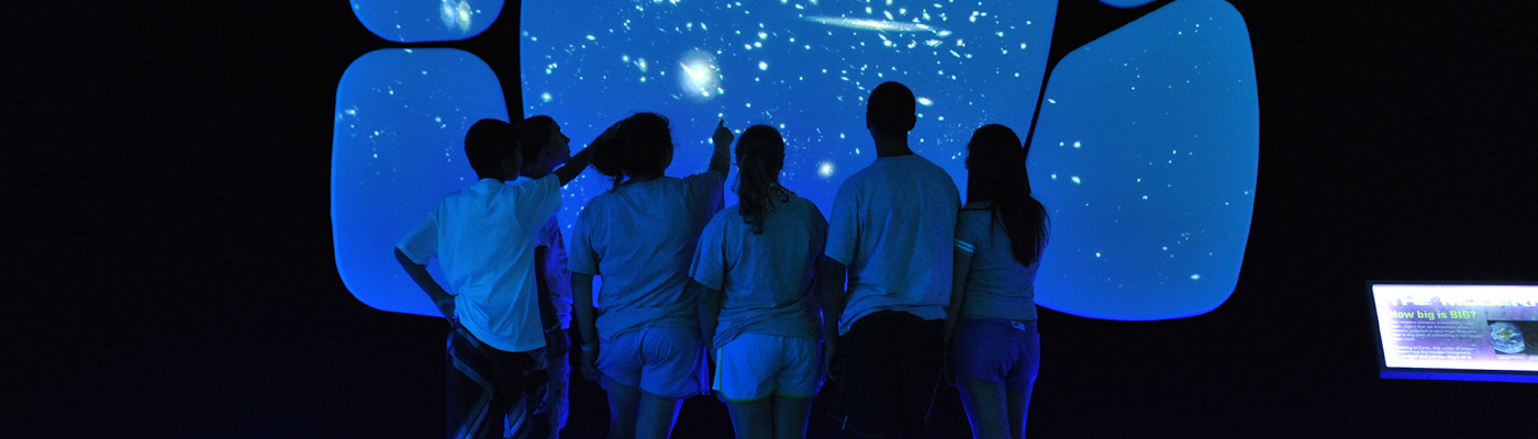 Students with their backs facing the camera point and take in the cosmic wall in the Universe exhibition