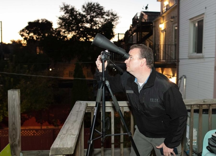 Man observes the night sky through a telescope in a back yard.
