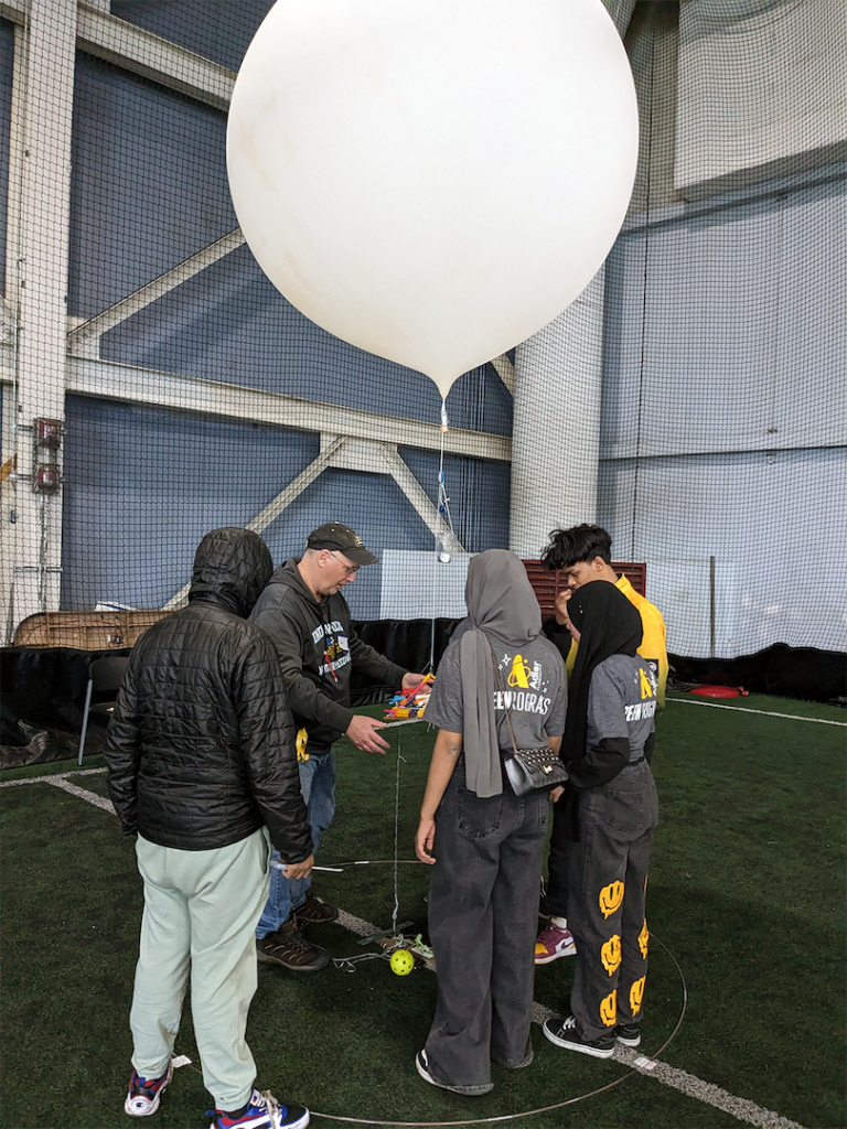 A team of students working with an Adler volunteer to attach their airship to a high-altitude balloon to complete a challenge.