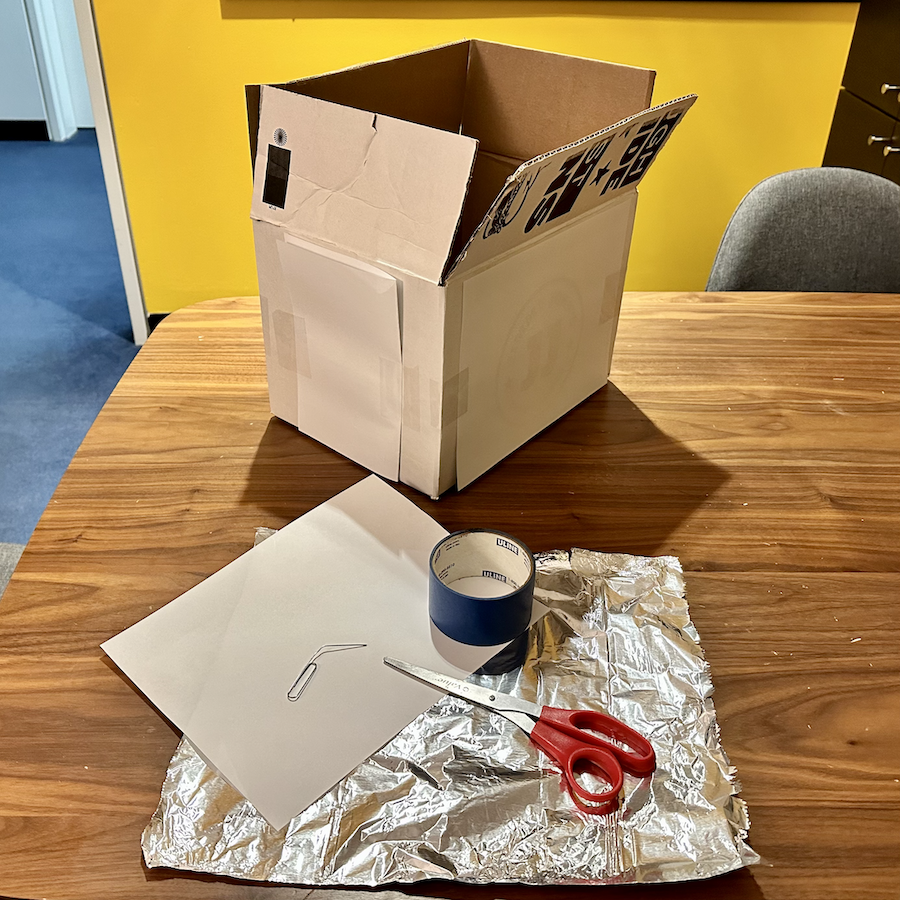 Supplies needed to build a pinhole projector to view a solar eclipse: a cardboard box, tape, a white piece of paper, aluminum foil, and a pin, nail or paperclip.