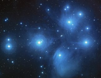 This is an image of the Pleiades star cluster. You can see in this image faint clouds of bluish nebulae and dozens of bright stars scattered in the distance.