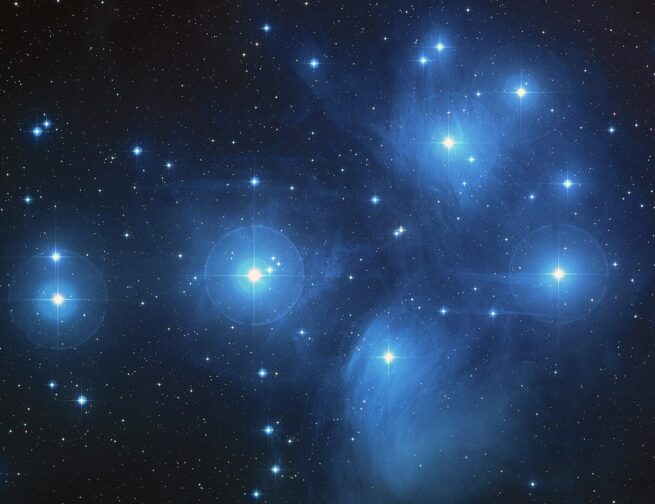 This is an image of the Pleiades star cluster. You can see in this image faint clouds of bluish nebulae and dozens of bright stars scattered in the distance.