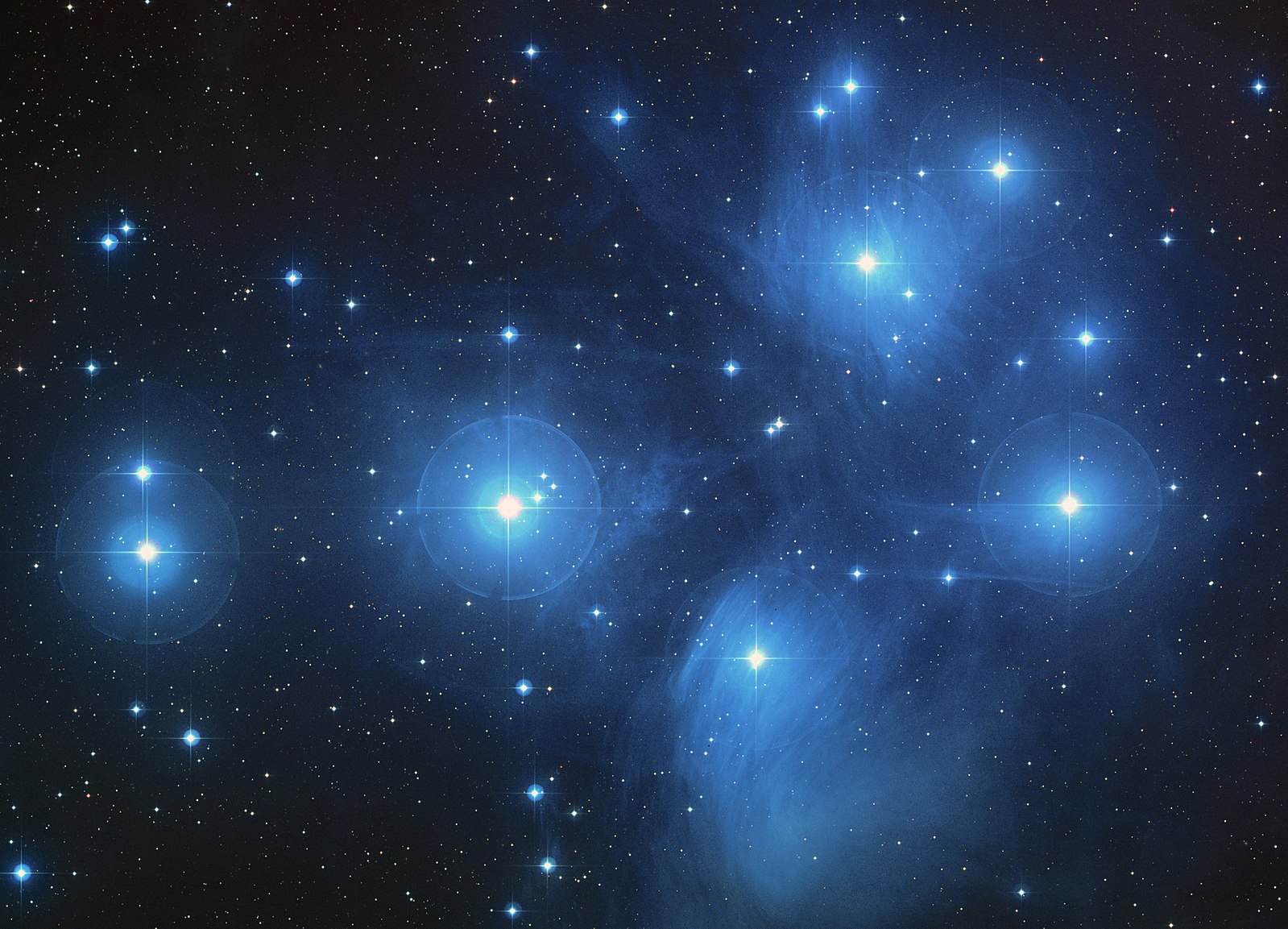 This is an image of the Pleiades star cluster. You can see in this image faint clouds of bluish nebulae and dozens of bright stars scattered in the distance.