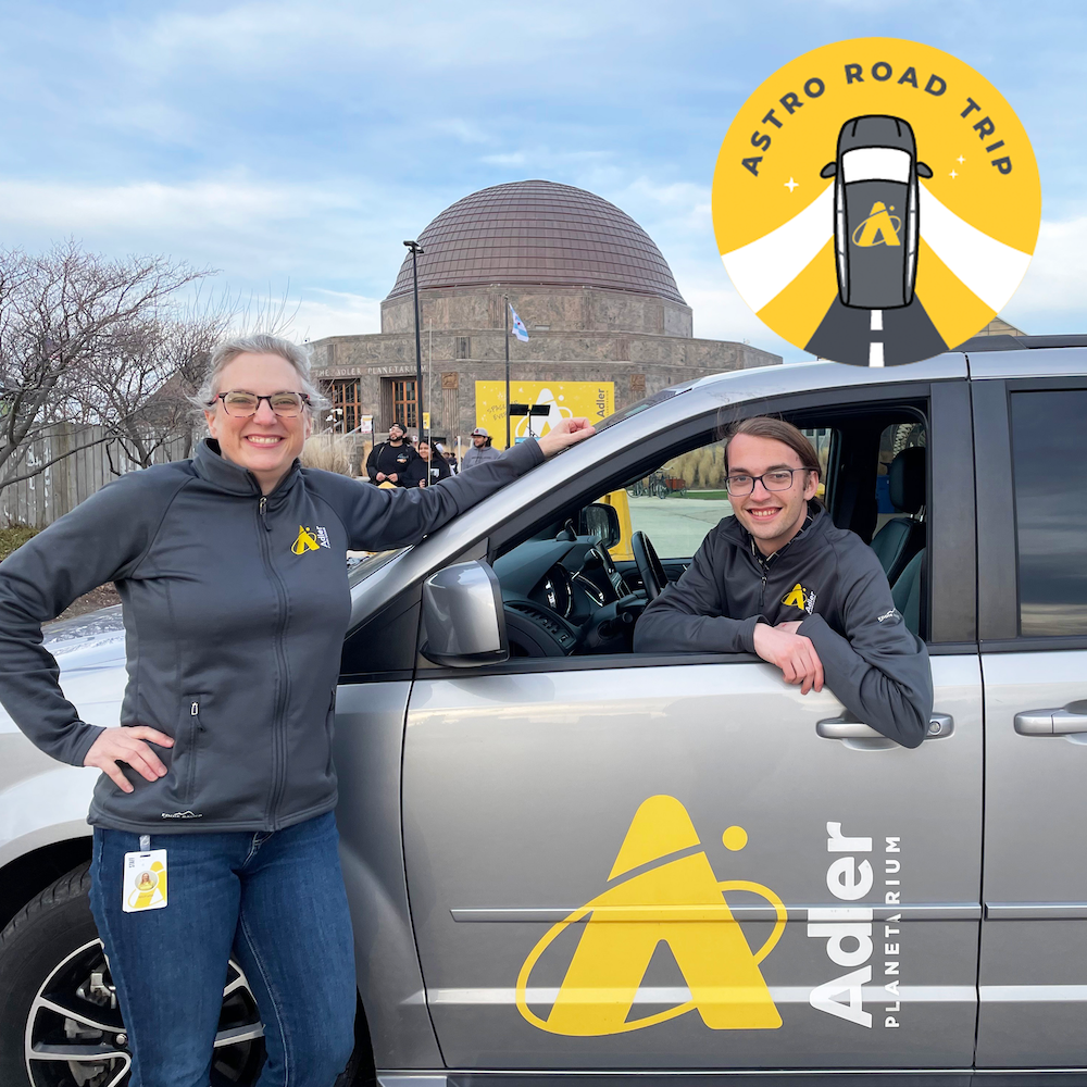 One person standing in front of a gray van with "Adler Planetarium" written on the van door and another person sitting inside the driver's seat of the van. In the background is the Adler Planetarium with a cloudy blue sky and a circular yellow logo with a gray car and "Astro Road Trip" written on it.