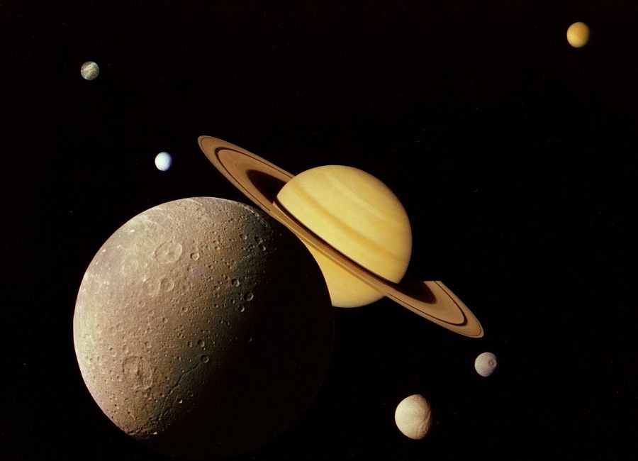 This montage of images of the Saturnian system was prepared from an assemblage of images taken by the Voyager 1 spacecraft during its Saturn encounter in November 1980. This artist's view shows Dione in the forefront, Saturn rising behind, Tethys and Mimas fading in the distance to the right, Enceladus and Rhea off Saturn's rings to the left, and Titan in its distant orbit at the top. The Voyager Project is managed for NASA by the Jet Propulsion Laboratory, Pasadena, California. Credit: NASA/JPL