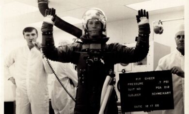 Robert Davidson, shown on the left of the image holding a microphone, seen here conducting a space suit fit check with Astonaut Rusty Schweikart on December 17, 1966.