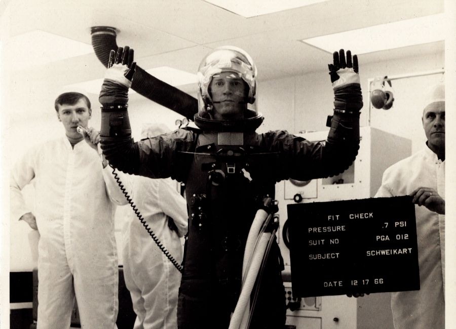 Robert Davidson, shown on the left of the image holding a microphone, seen here conducting a space suit fit check with Astonaut Rusty Schweikart on December 17, 1966.