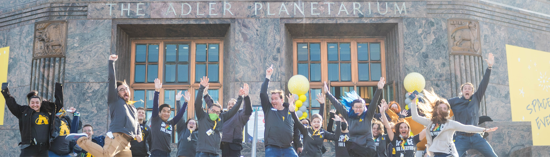 30 employees jumping on the stumps of the Adler smiling and celebratory with hands raised in the air and smiles