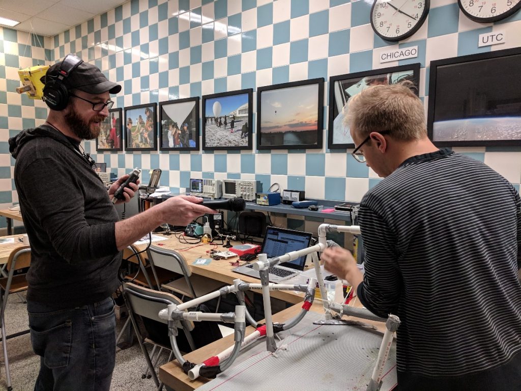 Project leader Chris Bresky (right) tries to reassemble a sled prototype from 2017 while podcast producer Erin Kahoa records.