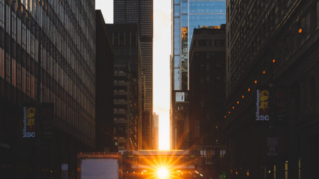 Pedestrians walking (during Chicagohenge) across a crosswalk while the Sun sets in the distance with the Willis Tower in view.
