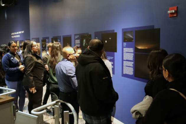 A crowd examines imagery of light pollution at an exhibition at the Adler Planetarium