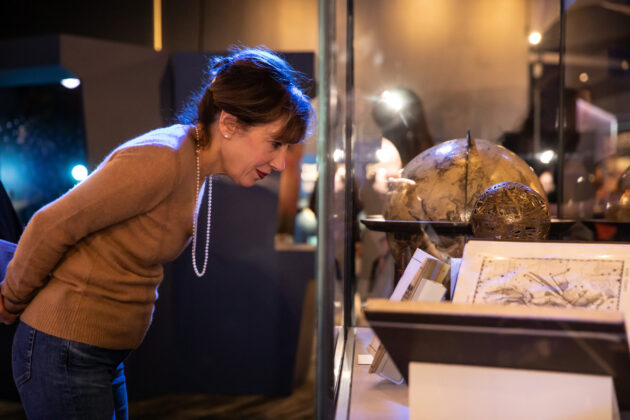 A woman leans in to read a placard on a glass case containing antique astronomy tools and texts