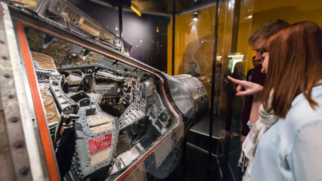 Two guests looking at the Gemini 12 spacecraft through glass