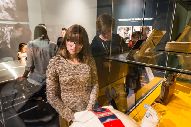 Two young people look at a space suit behind a glass case