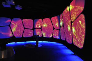 Inside the Adler Planetarium's exhibit, The Universe: A Walk Through Time and Space. Close up imagery of a red and yellow star appears on the exhibit screens. 