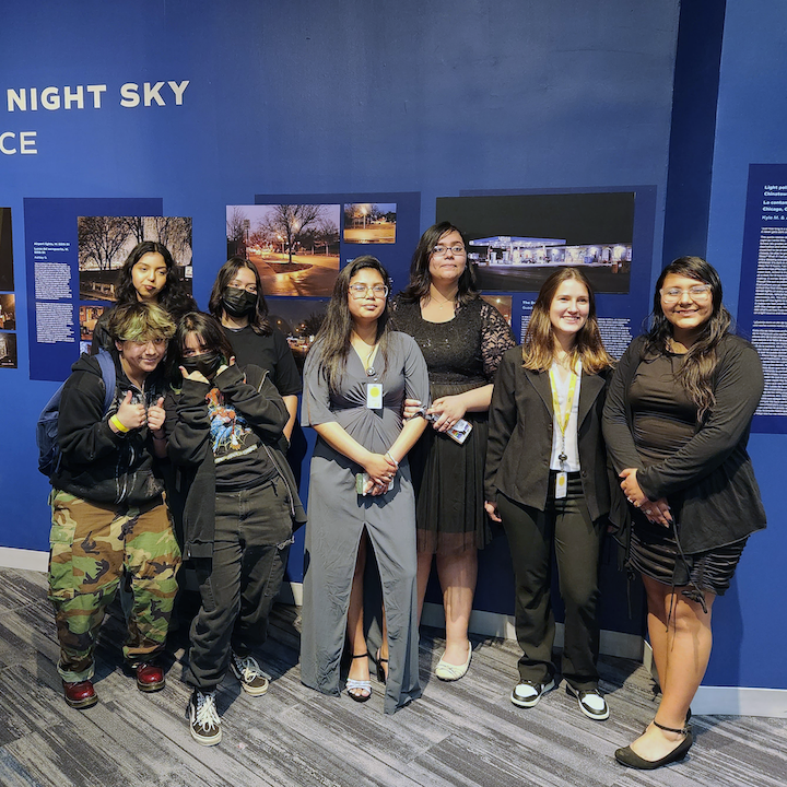 Youth Organization for Lights Out members and Teen Programs Manager, Waleska Valle, in front of the Little Village Night Sky exhibit.