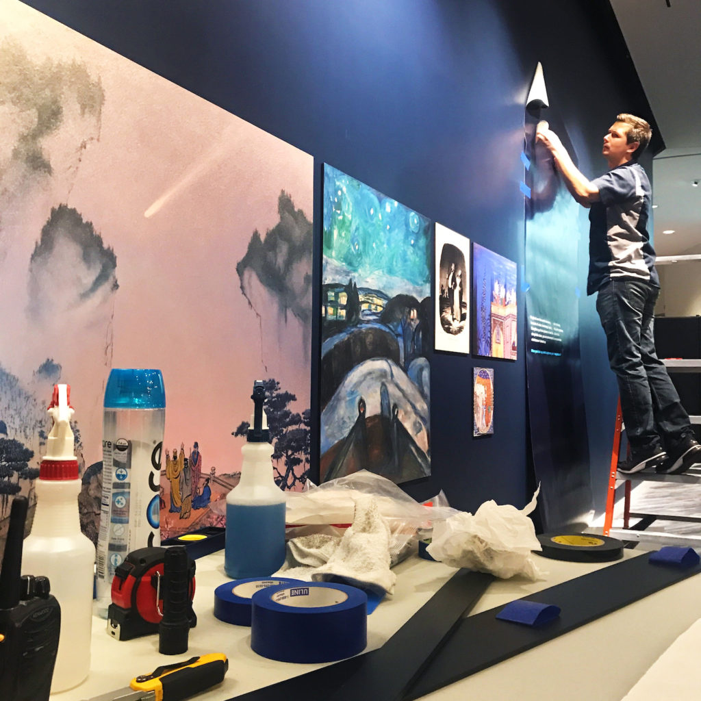 Neil Adam installing a graphic on a wall in The Adler Planetarium’s new exhibit, Chicago’s Night Sky.