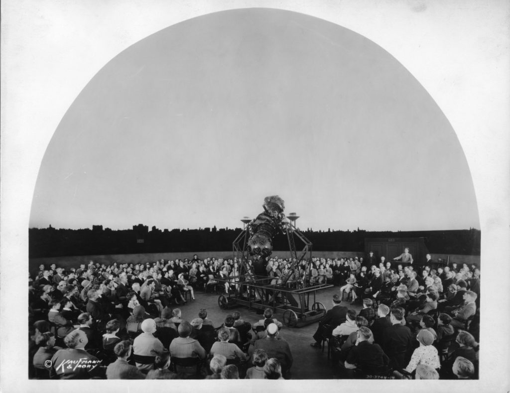 Image Caption: The Adler's first director, astronomer Philip Fox (standing up at the projector's control panel on the right) gets the audience ready for a demonstration with the Zeiss Mk II in the 1930s. Image Credit: Kaufmann & Fabry Co./Adler Planetarium Archives