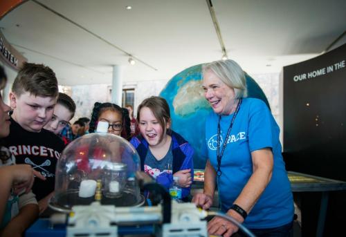 A volunteer smiles as she teaches young Adler guests about space science.